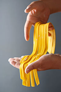 Cropped image of hands holding raw tagliatelle pasta against gray background