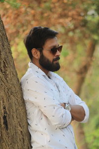 Young man wearing sunglasses standing by tree