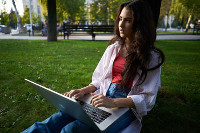 Young woman using laptop while sitting on field