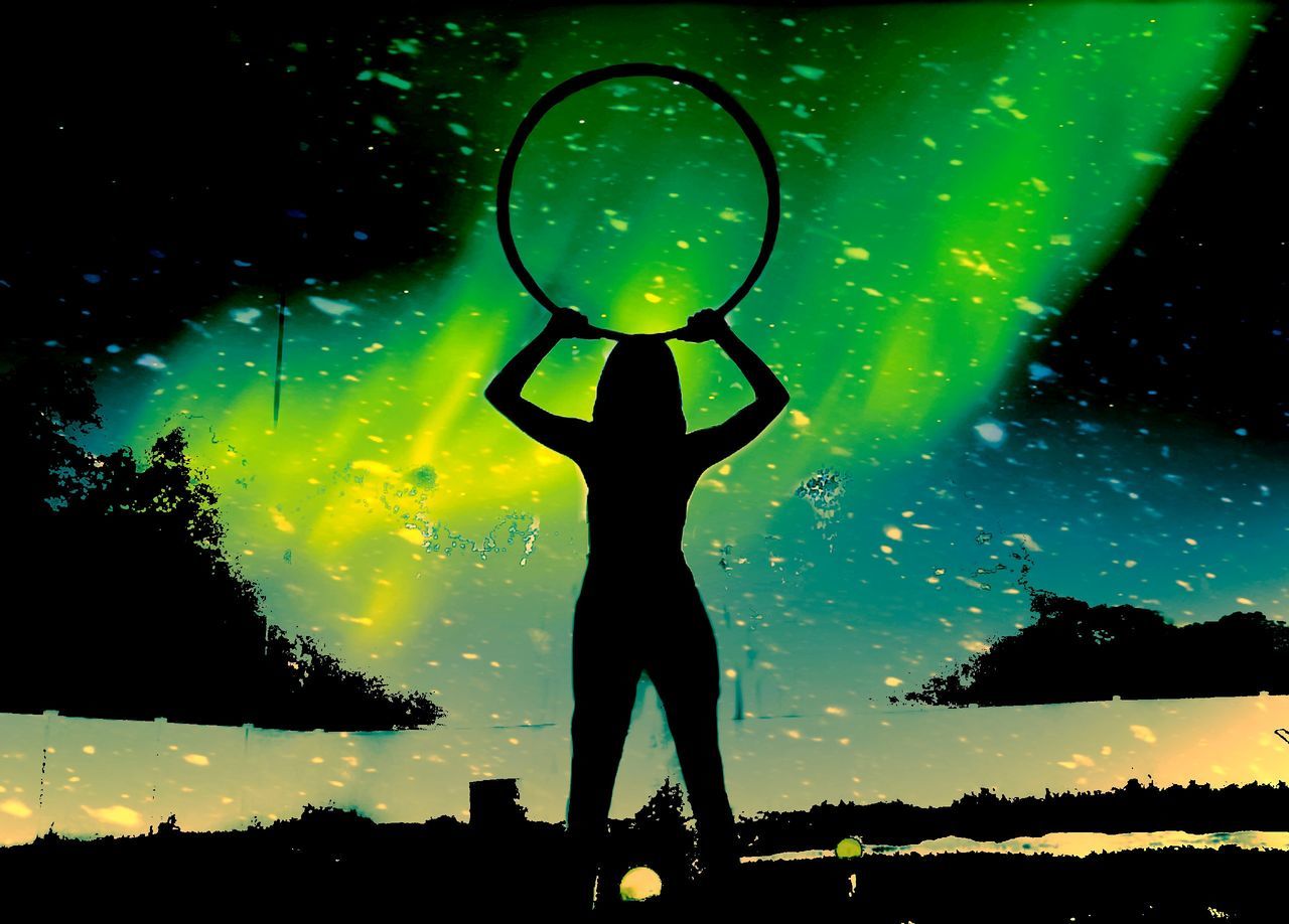 SILHOUETTE WOMAN STANDING ON ILLUMINATED FIELD AGAINST SKY AT NIGHT