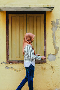Side view of woman wearing hijab standing against wall