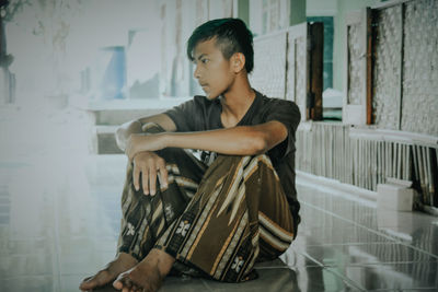 Young man looking away while sitting on seat in building