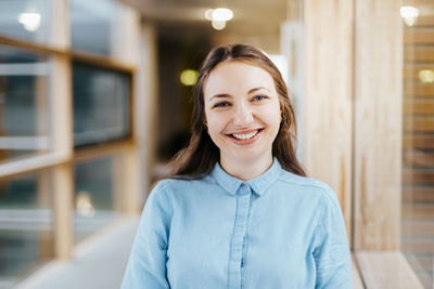 Portrait of happy young businesswoman standing at office corridor