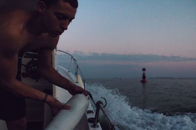 Shirtless man attaching buoy to boat railing in sea