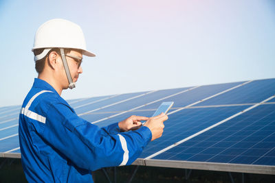 Side view of man using mobile phone against blue sky