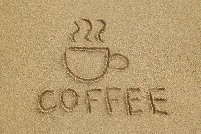 High angle view of text and coffee cup on carved in sand at beach