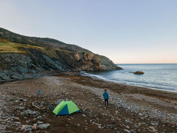 Rear view of man standing on beach with tent against sky