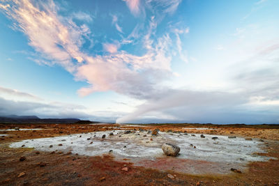 Wide view over a volcanic landscape with reddish and light gray ground, rising steam