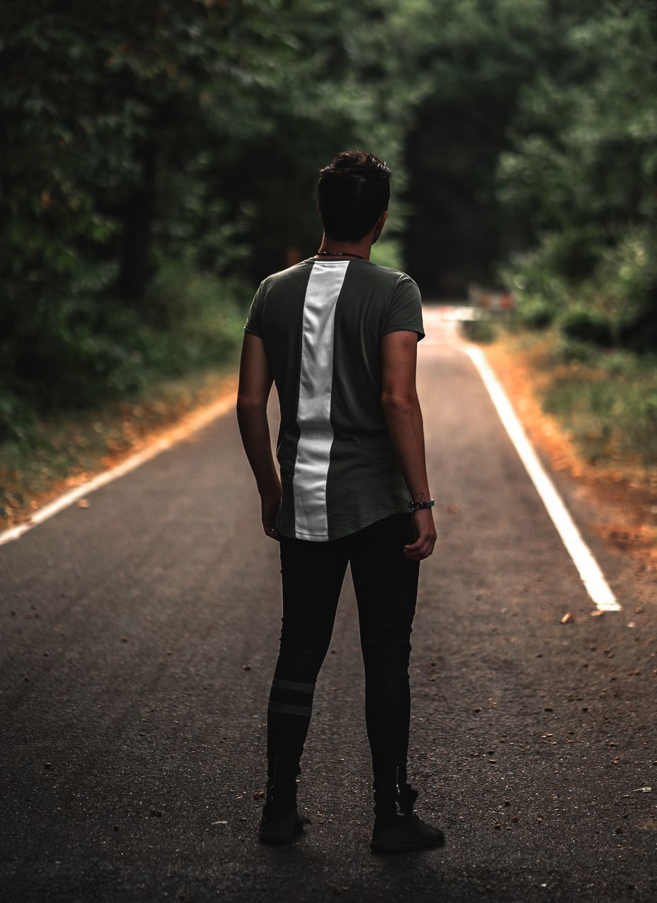 rear view, one person, full length, road, lifestyles, real people, casual clothing, standing, focus on foreground, leisure activity, young adult, men, direction, young men, the way forward, walking, transportation, tree, day, outdoors, hairstyle