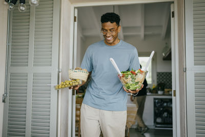 Smiling young man carrying food at doorway
