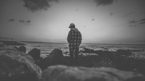 Rear view of man standing on rock at beach against sky