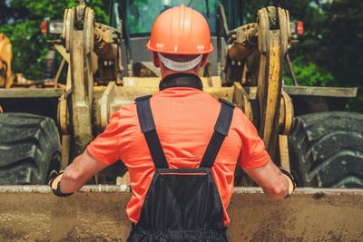 Rear view of worker standing by construction vehicle