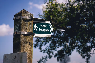 Low angle view of information sign on wooden post against sky