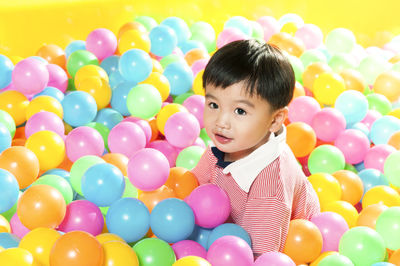 Portrait of smiling boy with colorful balloons against colored background