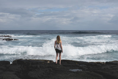 Rear view of woman standing on beach against sky