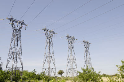 Low angle view of electricity pylons and trees against sky