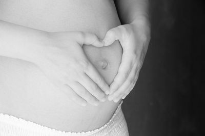 Midsection of pregnant woman making heart shape with hands on stomach