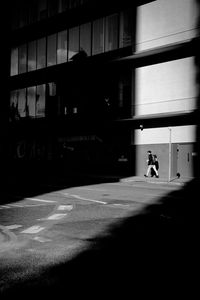 Silhouette person walking on street against building