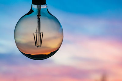 Close-up of light bulb hanging against sky at sunset