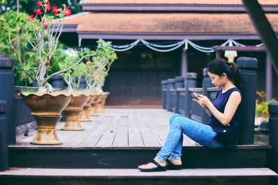 Side view of young woman using mobile phone while sitting outdoors