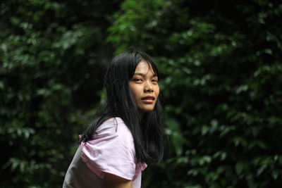 Portrait of beautiful young woman standing against trees