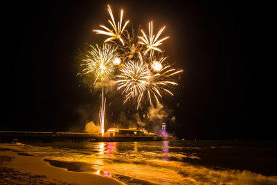 Low angle view of firework display over sea at night