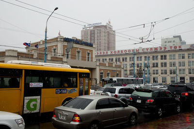Cars on road by buildings in city against sky