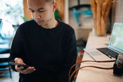 Young male photographer using smart phone sitting at table in cafe