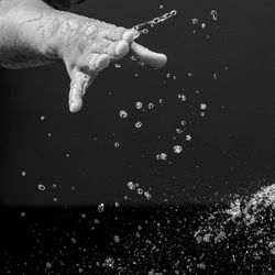 Close-up of hand holding water drop against black background