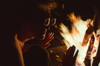 Man in protective eyewear by bonfire at night