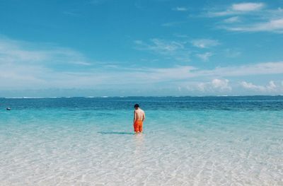 Rear view of man standing at beach against sky