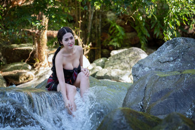 Young woman sitting by stream at forest