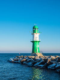 Lighthouse by sea against clear blue sky