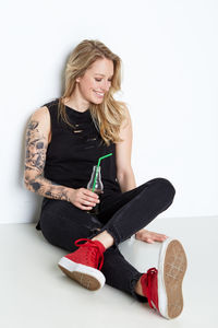 Smiling young woman sitting against white wall