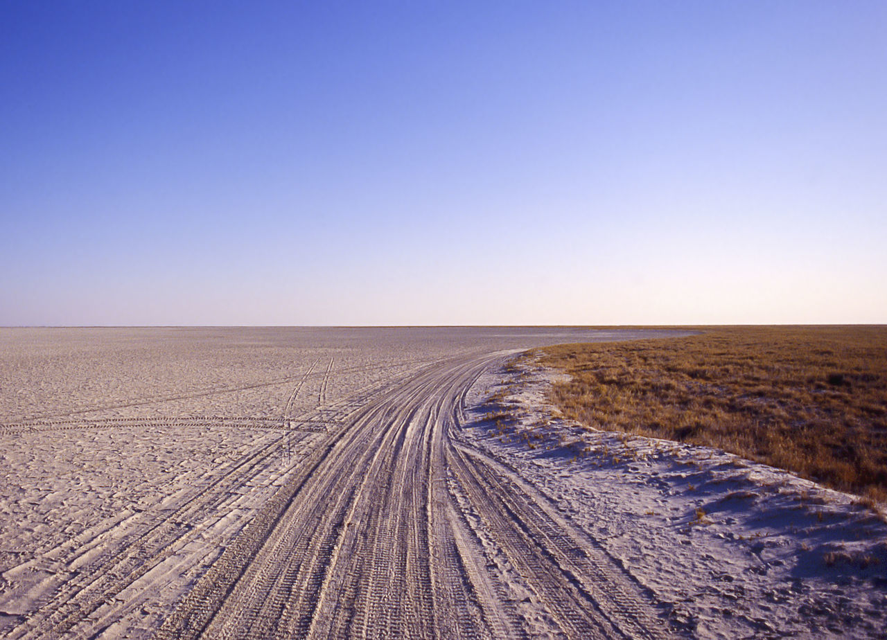 sky, copy space, clear sky, environment, landscape, land, nature, tranquil scene, scenics - nature, tranquility, beauty in nature, day, horizon, horizon over land, no people, field, desert, blue, tire track, non-urban scene, outdoors, diminishing perspective, climate, arid climate