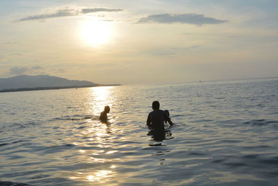 Silhouette men in sea against sky during sunset