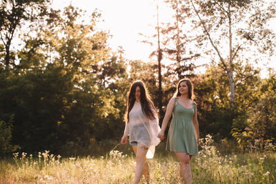 Lesbian couple holding hands while standing in forest in summer