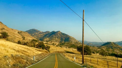 Country road leading towards mountains against sky