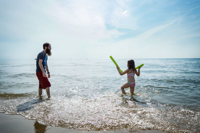 Father with daughter standing on shore at beach against sky