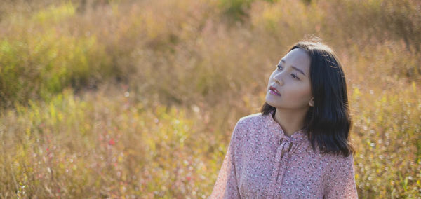 Young woman looking away while standing on field