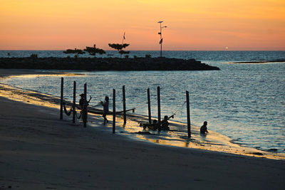 Silhouette birds at beach against sky during sunset