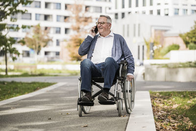 Smiling senior man talking on mobile phone sitting on wheelchair
