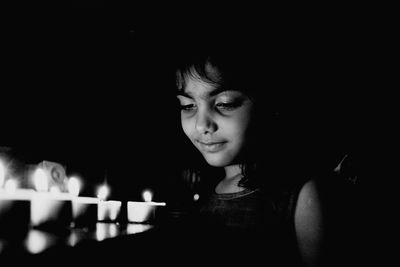 Close-up of cute girl looking at illuminated tea lights at night