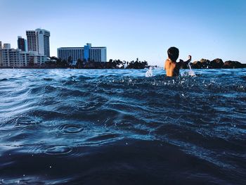 Rear view of boy in river against clear sky