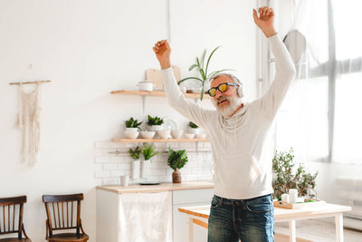 Rear view of woman with arms raised standing at home