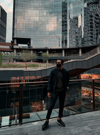 Full length of man standing by railing against buildings in city