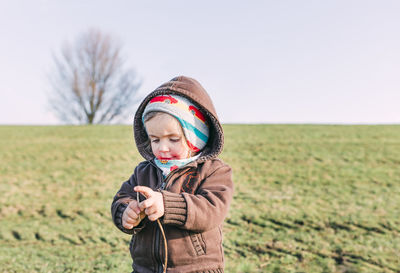 Cute girl holding stick while standing on grassy field against sky