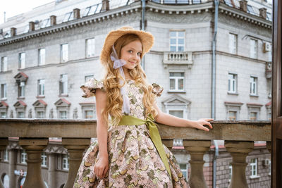 Little girl in dress and hat posing on the balcony