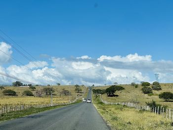 Road amidst field against clear blue sky