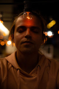 Close-up of man with eyes closed by light bulb